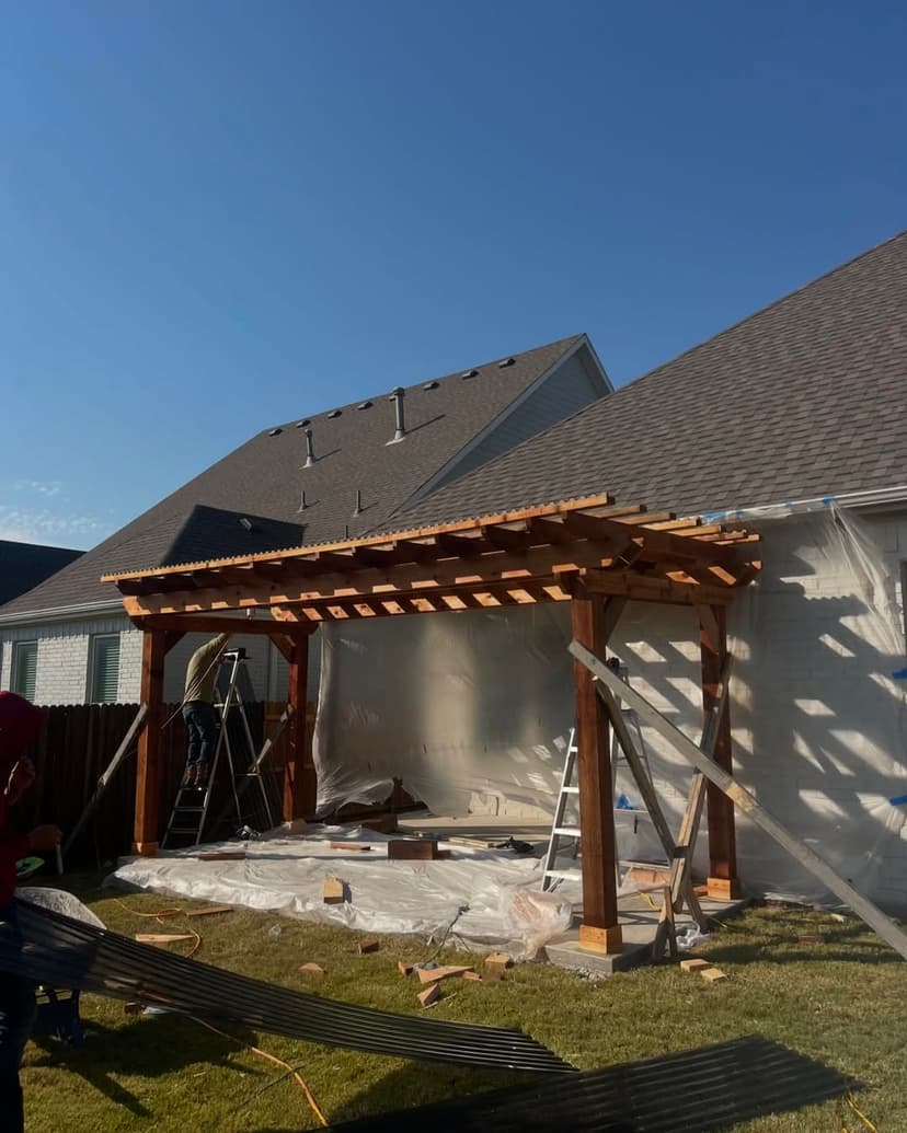 Wooden pergola under construction in backyard with scaffolding and plastic sheeting.