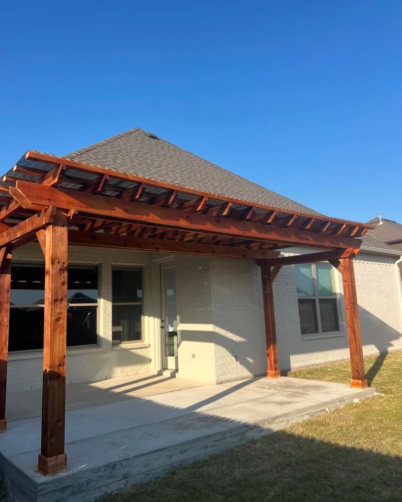 Wooden pergola attached to a house with a yard under a clear blue sky.