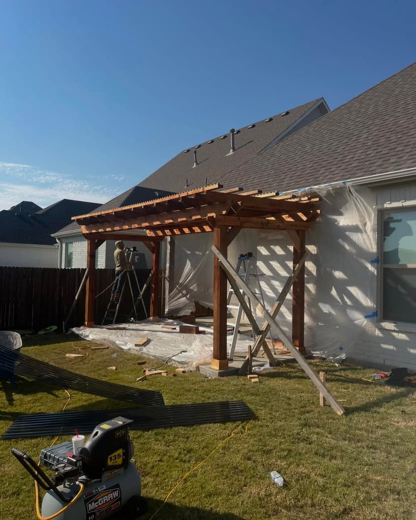 Wooden pergola under construction next to a house, with tools and scaffolding visible.